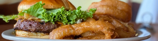 A burger on a bun with large fluffy lettuce next to a side of crispy onion rings