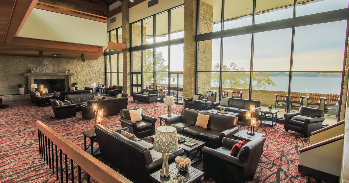 A large shared space with leather couches and chairs, a fire place, and floor-to-ceiling windows overlooking the lake